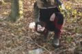 knieende blondhaarige Försterin Wald mit Müll in den Händen, den sie in die Kamera hält